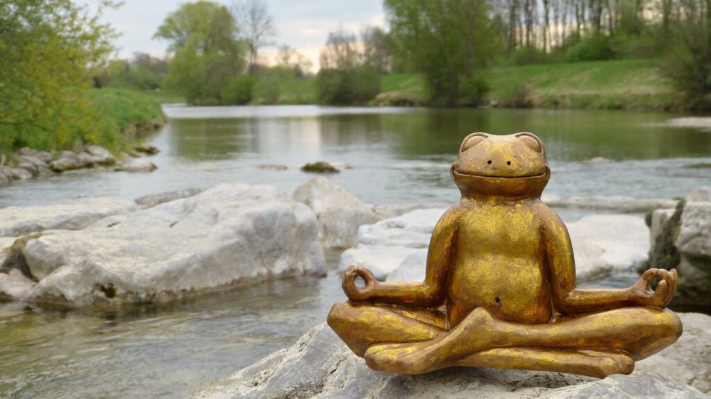 bronze frog in lotus position on a rock in a stream.